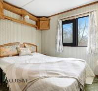 Hálószoba egy faházban virágos kiegészítőkkel, egy ablakkal és fa bútorokkal.