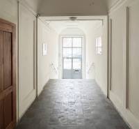 Csempeburkolatú és fehér falú folyosó vezet az üvegezett kapuhoz a Vajnorská utcán.