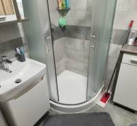 Fürdőszoba sarokzuhannyal, mosdóval és szekrénnyel egy kétszobás lakásban.