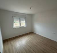 Szoba egy háromszobás lakásban, fa dekoros padlóval és fehér falakkal.