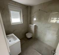 Fürdőszoba egy háromszobás lakásban mosdóval, WC-vel és üvegfalú zuhanyzóval.