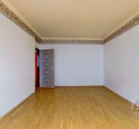 Szoba egy háromszobás lakásban, fa dekorációjú padlóval és fehér falakkal.