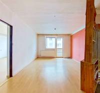 Tágas belső tér háromszobás lakásban fa mintázatú padlóval és erkéllyel.