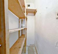 Keskeny kamra fa polcokkal egy háromszobás lakásban, fehér falakkal.