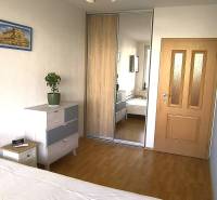 Hálószoba beépített szekrénnyel, fa dekor padlóval, szekrény, ágy, csillár, növény.