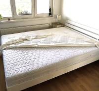 Világos hálószoba fehér ággyal és fa dekorációjú padlóval egy kétszobás lakásban.