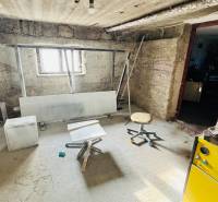 Rodinný ház alagsori helyisége egyszerű bútorokkal és ablakkal.