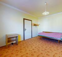 Szoba családi házban ággyal, asztalkával és mintás szőnyeggel.