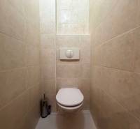 Fehér csempével burkolt és beépített WC-vel rendelkező toalett egy háromszobás lakásban.