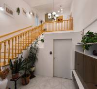 Egy családi ház belső terében található egy fa lépcső, növények és világítótestek.