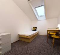 Egyszerű szoba egy ággyal, asztallal és komóddal egy családi házban.