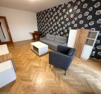 Nappali egy háromszobás lakásban fa mintázatú padlóval, mintás tapétával és bútorokkal.