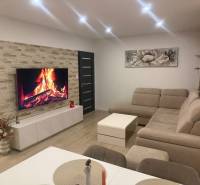 Nappali egy háromszobás lakásban sarokkanapéval és fa mintázatú padlóval.