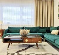 Családi ház zöld árnyalatú kanapéval, fa bútorokkal és művészettel a falon.