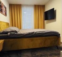 Hálószoba családi házban ággyal, éjjeliszekrénnyel, TV-vel és függönyökkel.