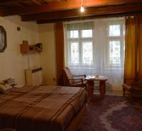 Szoba családi házban ággyal, székekkel, sárga függönyökkel és szőnyeggel.