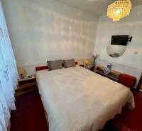 Hálószoba egy háromszobás lakásban ággyal, csillárral és a falon lévő televízióval.