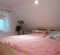 Tetőtéri hálószoba családi házban, ággyal, televízióval és fa dekorációjú padlóval.