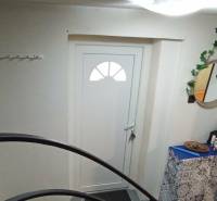 Családi ház bejárata fehér ajtókkal, tükörrel és dekoratív elemekkel.