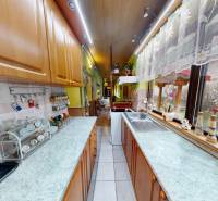 Családi ház konyhája szekrényekkel, készülékekkel és kilátással a kertre egy nagy ablakon keresztül.