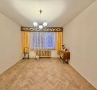 Szoba egy háromszobás lakásban fa dekoros padlóval, függönyökkel és komóddal.