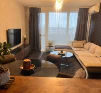 Nappali fa mintás padlóval, kanapéval és televízióval egy kétszobás lakásban.