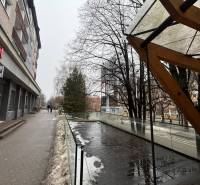 Üzlethelyiségek Poprádon, üvegkorláttal és nedves csempével szomszédos, havas járda.