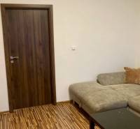 Nappali kanapéval, fa dekor padlóval és sötét ajtókkal egy háromszobás lakásban.