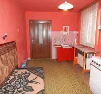 Családi ház konyhája piros falakkal, régebbi bútorokkal és zöld szőnyeggel.