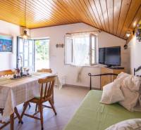 Nyaraló apartman étkező sarokkal, televízióval, nyitott ablakkal és fa mennyezettel.