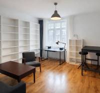 2 szobás lakás belső tere fa hatású padlóval, nagy polcokkal és modern bútorokkal.