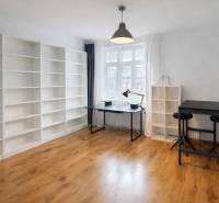 Tágas szoba polcokkal, asztallal és fa dekorációjú padlóval egy kétszobás lakásban.