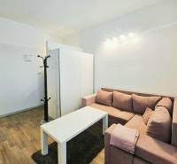 Garzonlakás sarokkanapéval, fehér asztallal és fa dekorációjú padlóval.