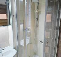 Fürdőszoba üveg zuhanykabinnal és világos csempékkel a garzonlakásban.