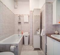 Fürdőszoba egy egyszobás lakásban káddal, mosdóval és semleges árnyalatú kerámia burkolatokkal.