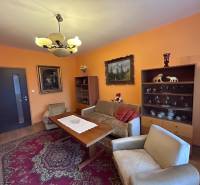 Nappali egy kétszobás lakásban narancssárga falakkal, dekoratív szőnyeggel és fa mintázatú padlóval.