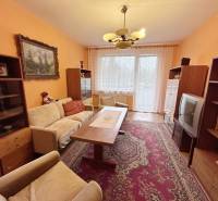 Nappali egy kétszobás lakásban régebbi bútorokkal, szőnyeggel és dekoratív függönyökkel.