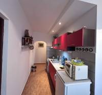 Konyha piros szekrényekkel és fa dekoros padlóval egy kétszobás lakásban.