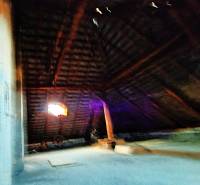 Családi ház tetőtéri szobája fa gerendákkal és ablakkal.