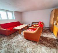 Nappali egy családi házban narancssárga kanapéval, fa asztallal és vitrinnel.