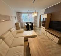 Nappali fa dekor padlóval, nagy kanapéval és étkezőasztallal egy háromszobás lakásban.