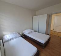 Szoba egy családi házban két ággyal, szekrénnyel és fa mintázatú padlóval.