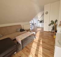 Családi ház tetőtéri nappalija kanapéval, étkezőasztallal és fa dekorációjú padlóval.