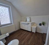 Fürdőszoba fa dekoros padlóval egy családi házban, WC-vel, mosdóval és káddal felszerelve.