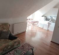 Családi ház tetőtéri helyisége konyhával, virágmintás kanapéval és fa dekorációjú padlóval.