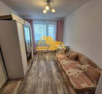 Szoba egy háromszobás lakásban kanapéval, szekrénnyel és fa dekor padlóval.