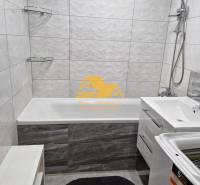 Fürdőszoba egy háromszobás lakásban káddal, zuhanyzóval és mosógéppel fehér csempéken.