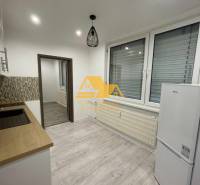 Konyha egy egyszobás lakásban, fa dekor padlóval és fehér háztartási gépekkel.