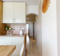 Konyhapult fehér szekrényekkel és fa dekorációjú padlóval egy háromszobás lakásban.