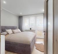 Hálószoba egy háromszobás lakásban ággyal, függönyökkel és fa dekorációjú padlóval.